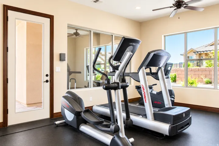 Rubber mat flooring, large windows, ceiling fan, and mirrored wall