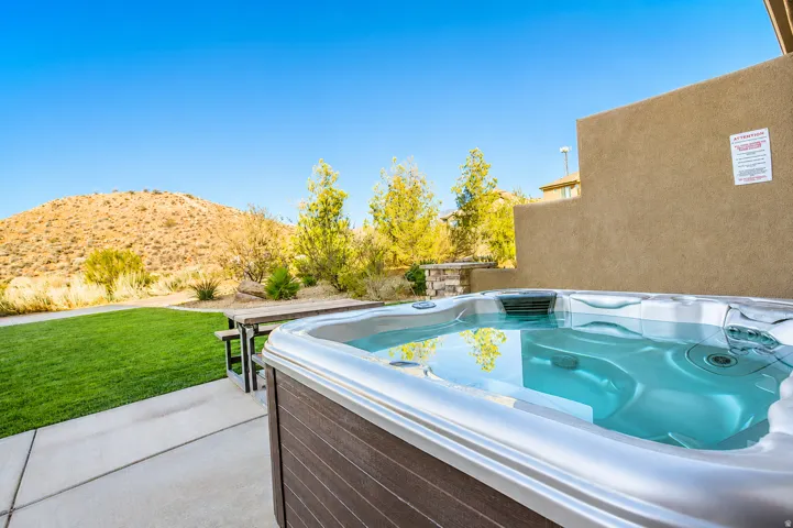 Outdoor spa, concrete patio, and manicured lawn with natural landscaping