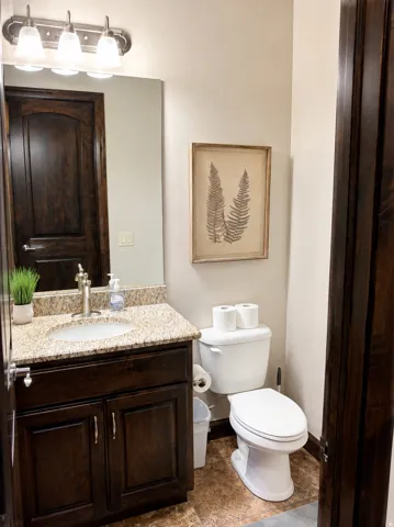 Granite-finish countertop with an undermount sink, dark wood-finish cabinetry, and a full wall mirror with a four-light fixture