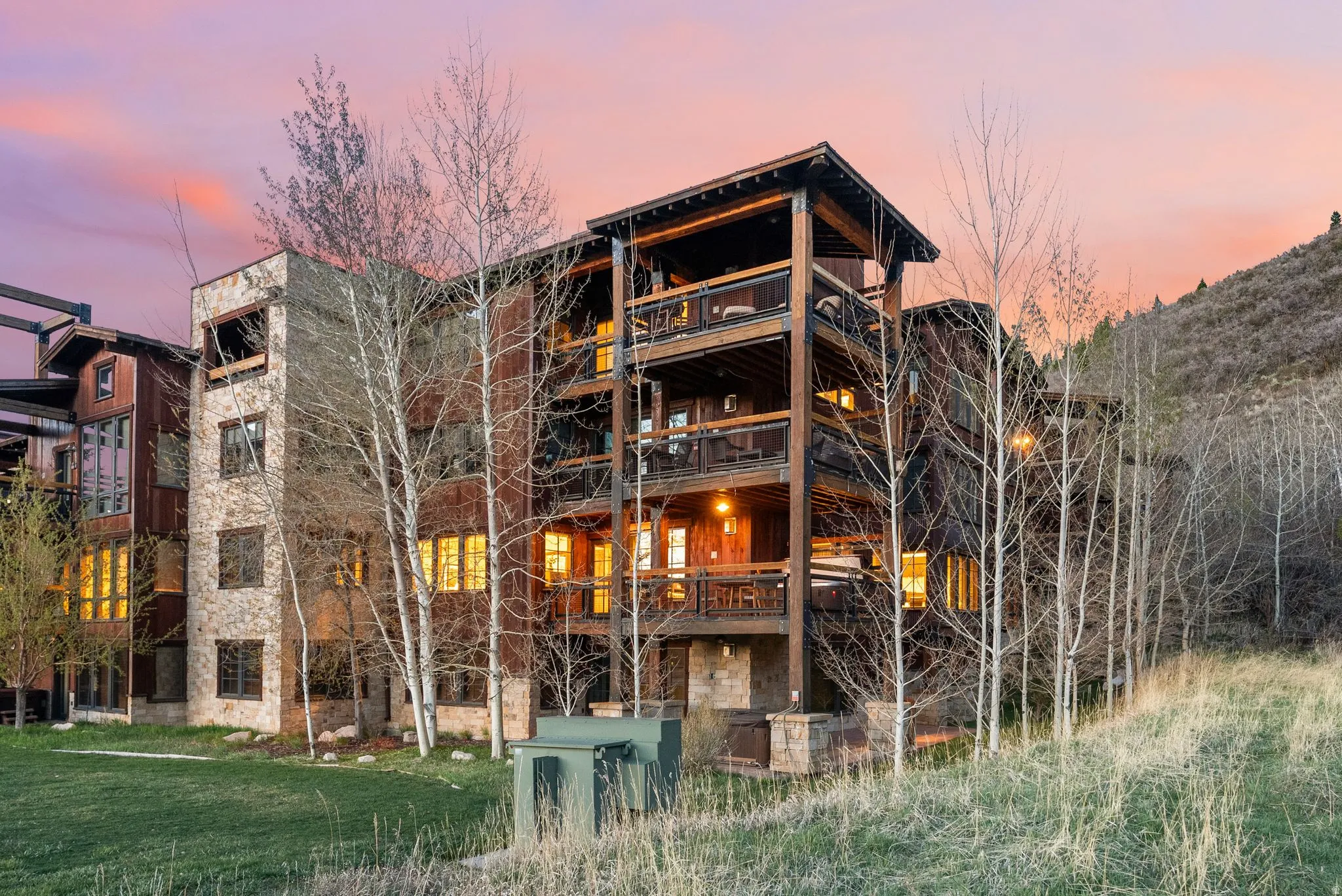 Back of house at dusk featuring stone siding and a lawn