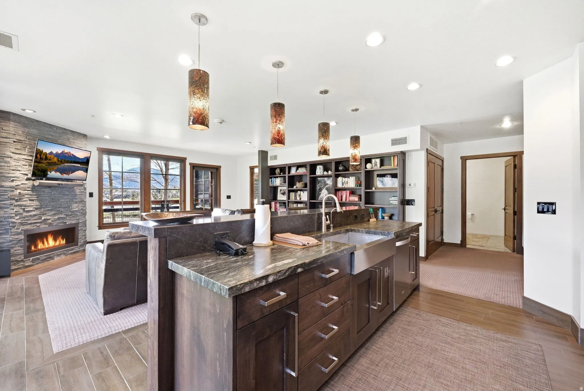 Kitchen featuring dark wood finish cabinets, a stone fireplace, open floor plan, wood tiled floors, and pendant lighting