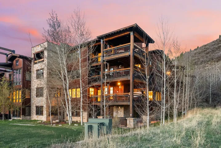 Back of house at dusk featuring stone siding and a lawn