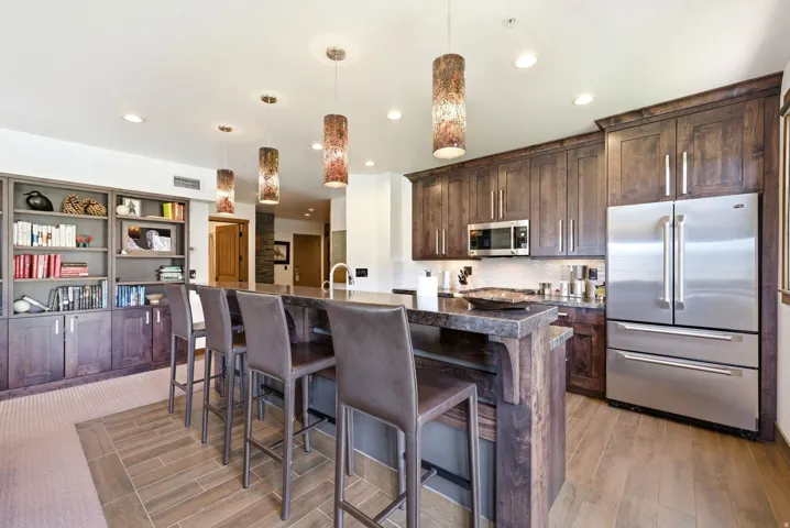 Kitchen with stainless steel appliances, a center island with sink, dark wood finish cabinets, a kitchen bar, and decorative light fixtures