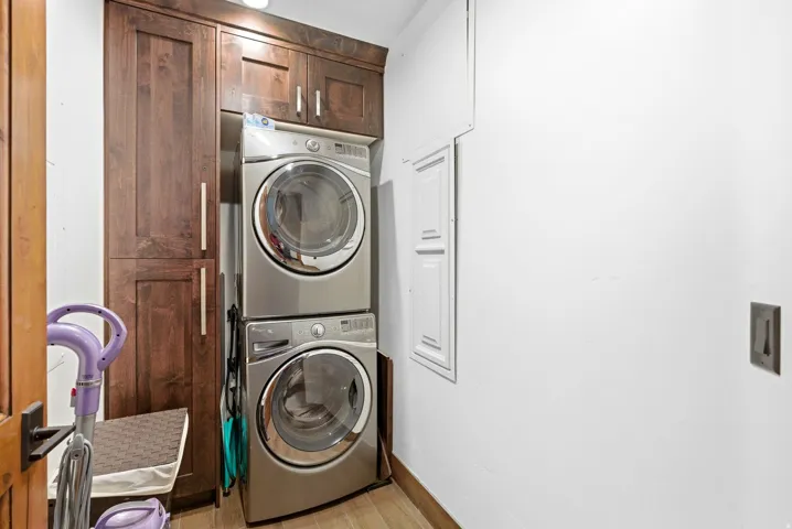 Laundry area with light wood-type flooring, stacked washer / dryer, and cabinet space