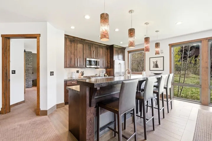 Kitchen featuring dark wood finish cabinets, a kitchen breakfast bar, an island with sink, decorative light fixtures, and dark stone counters
