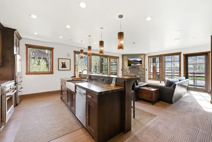 Kitchen featuring dark wood finish cabinets, a breakfast bar area, an island with sink, decorative light fixtures, and stainless steel appliances