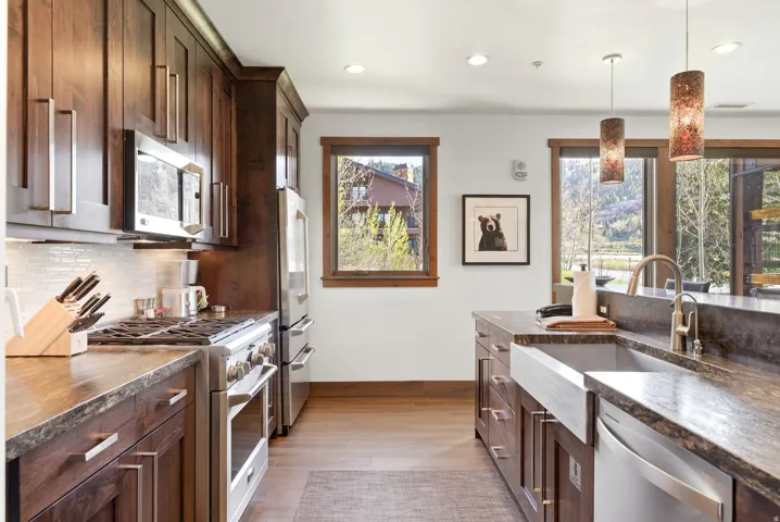 Kitchen with stainless steel appliances, dark wood finish cabinets, dark stone countertops, and decorative light fixtures