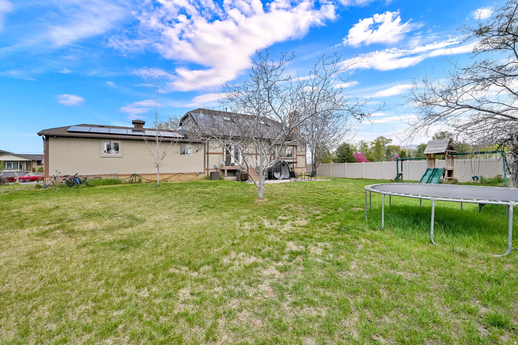 Rear view of house with a trampoline, a fenced backyard, a playground, stucco siding, and roof mounted solar panels