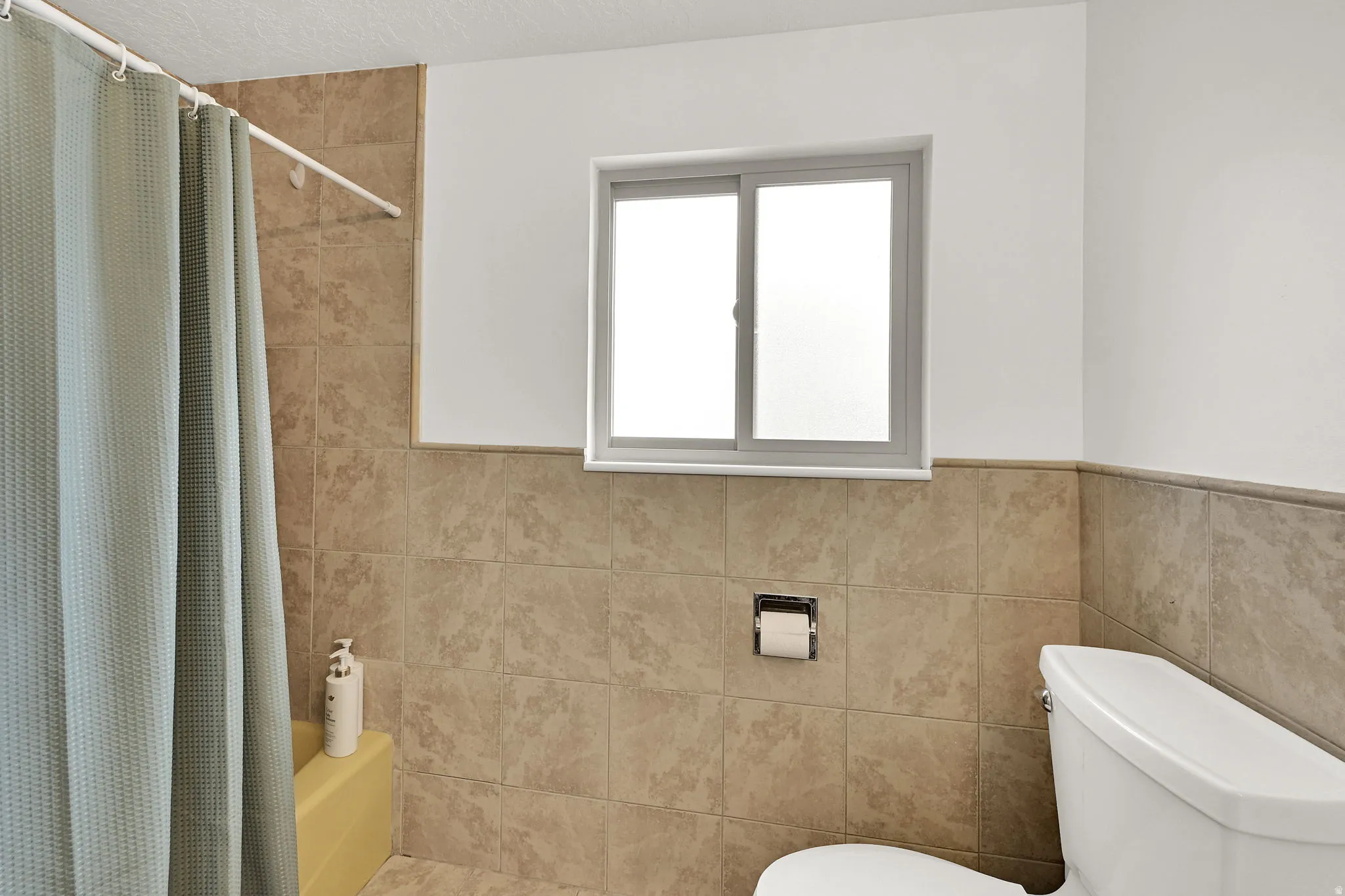 Bathroom featuring shower / bath combination with curtain, tile walls, and wainscoting