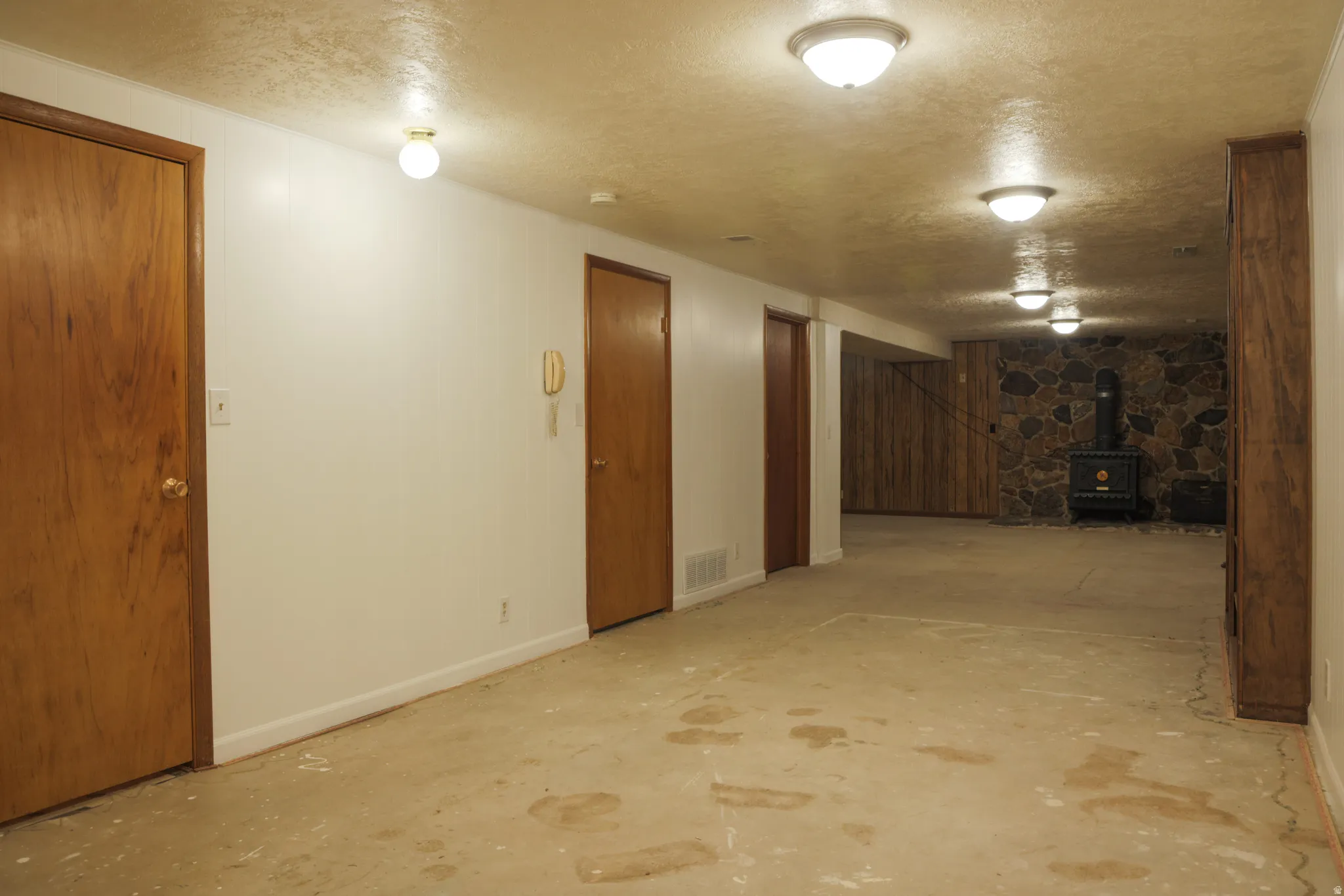 Finished basement featuring a textured ceiling, a wood stove, and wooden walls