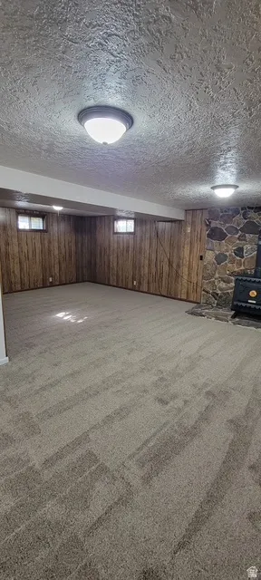 Basement with carpet floors, a wood stove, and a textured ceiling