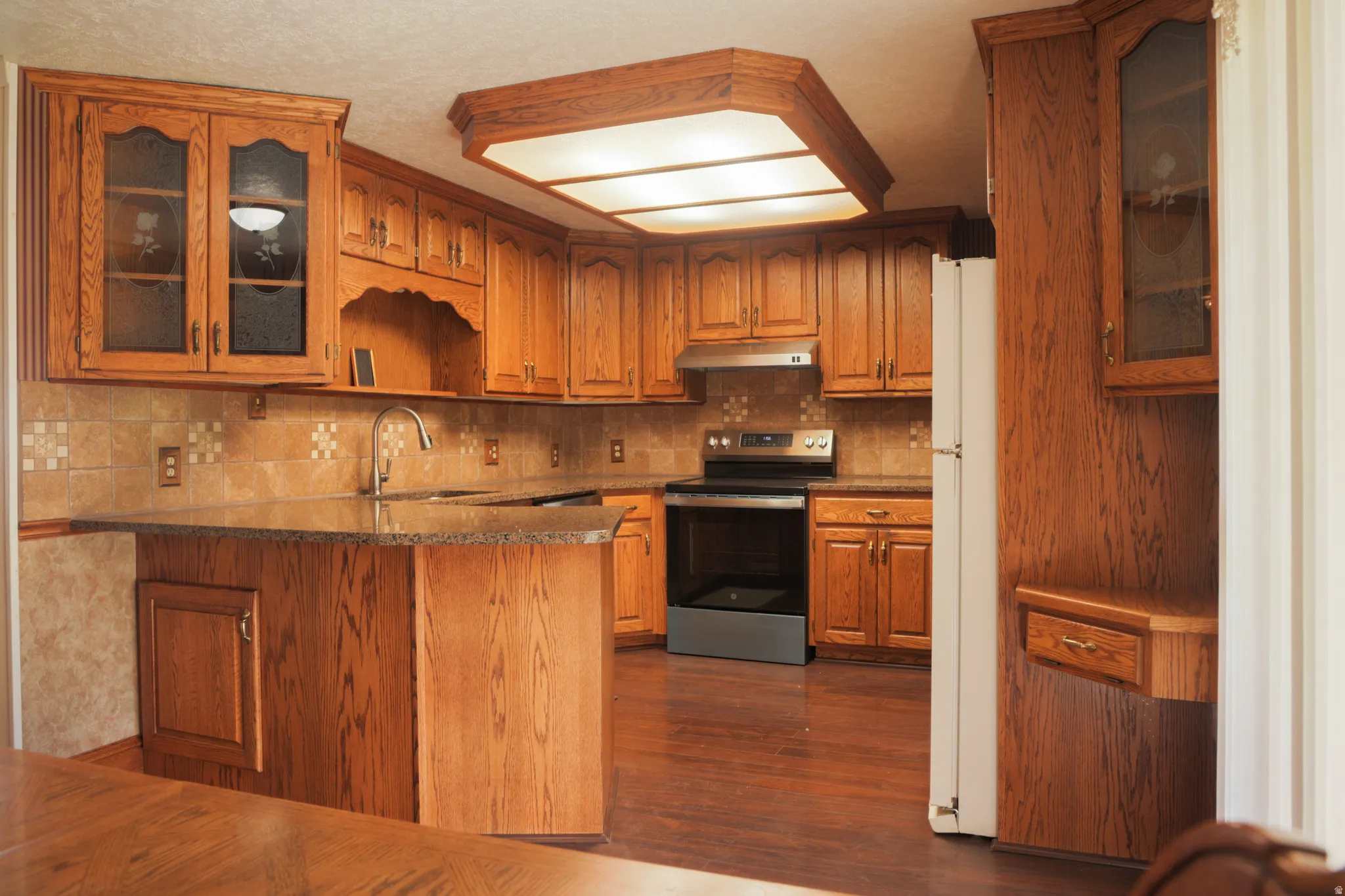 Kitchen featuring glass insert cabinets, stainless steel electric stove, wood finish cabinets, a peninsula, and freestanding refrigerator