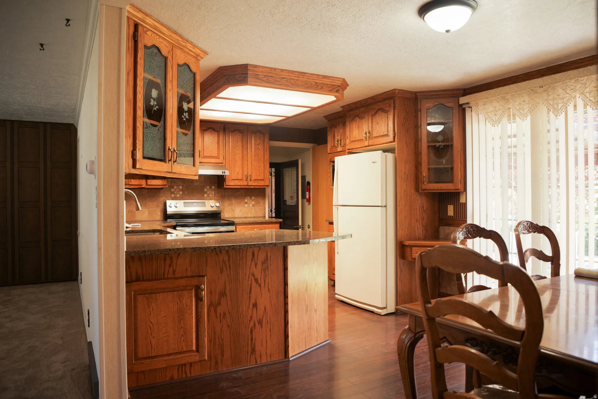 Kitchen with glass fronted cabinets, freestanding refrigerator, stainless steel electric stove, a peninsula, and wood finish cabinets