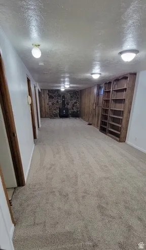 Finished basement featuring a textured ceiling, a wood stove, and light carpet