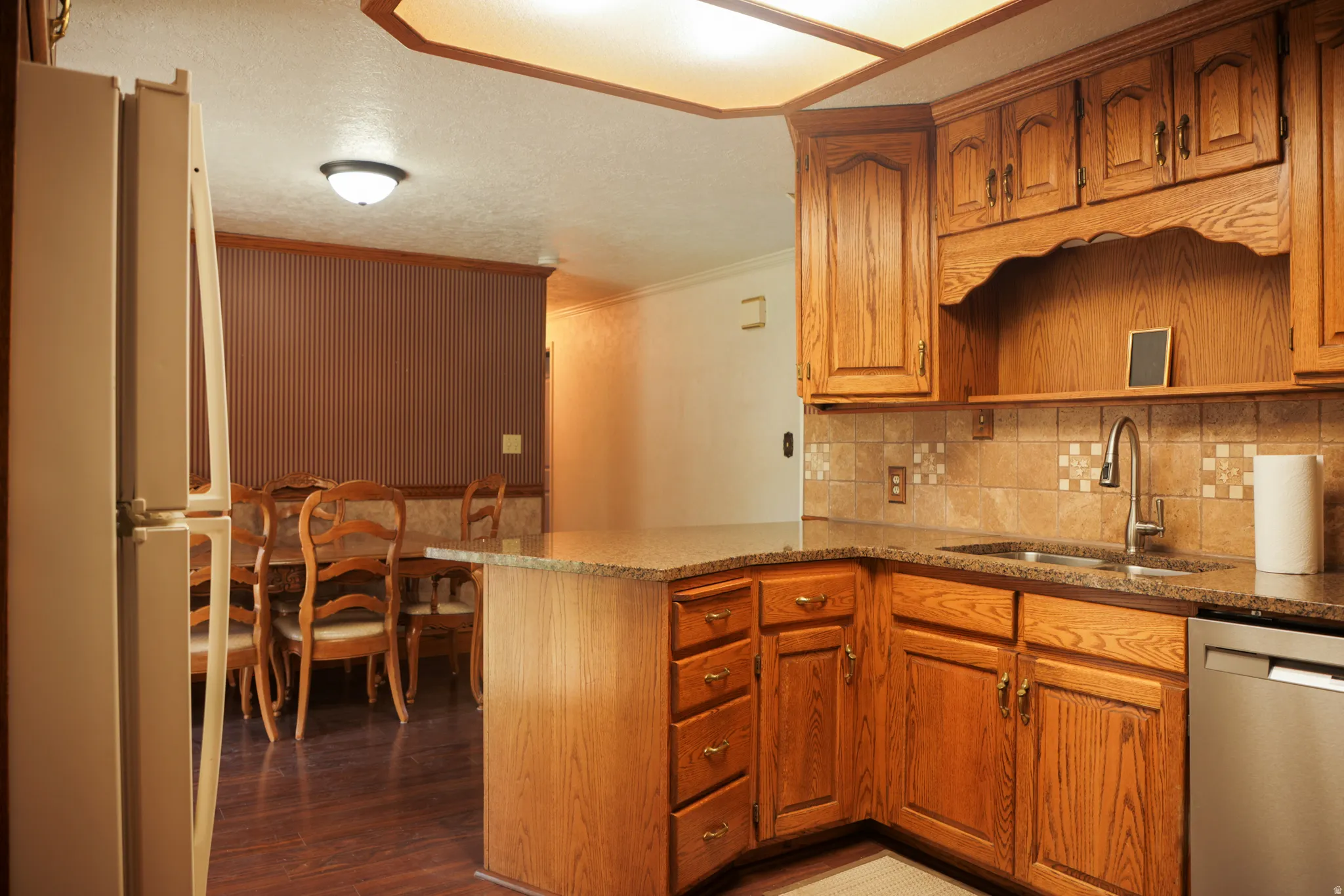 Kitchen with freestanding refrigerator, ornamental molding, dark stone counters, wood finish cabinetry, and stainless steel dishwasher