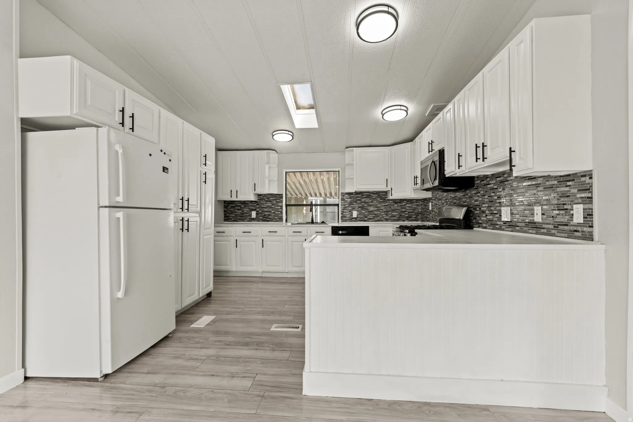 Kitchen with stainless steel appliances, light countertops, white cabinets, a peninsula, and backsplash