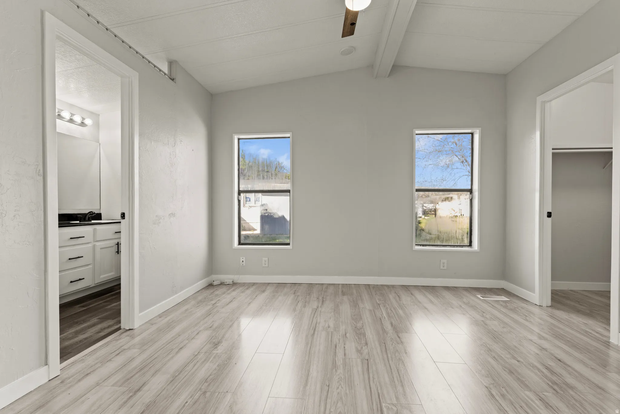 Unfurnished bedroom with a walk in closet, vaulted ceiling with beams, light wood-style flooring, ceiling fan, and connected bathroom