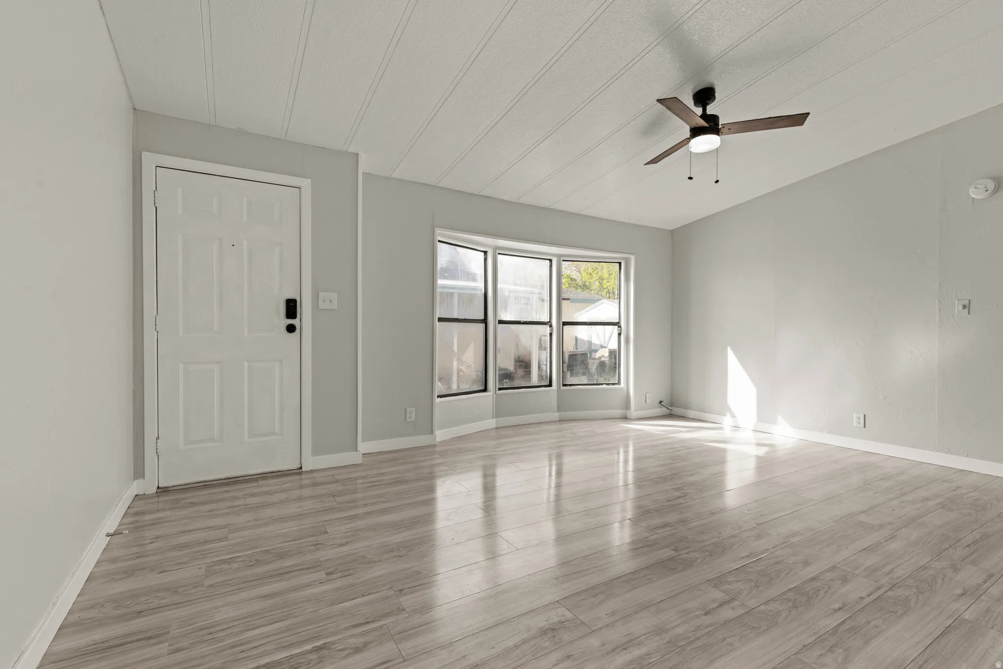 Unfurnished living room featuring light wood finished floors, a ceiling fan, and vaulted ceiling