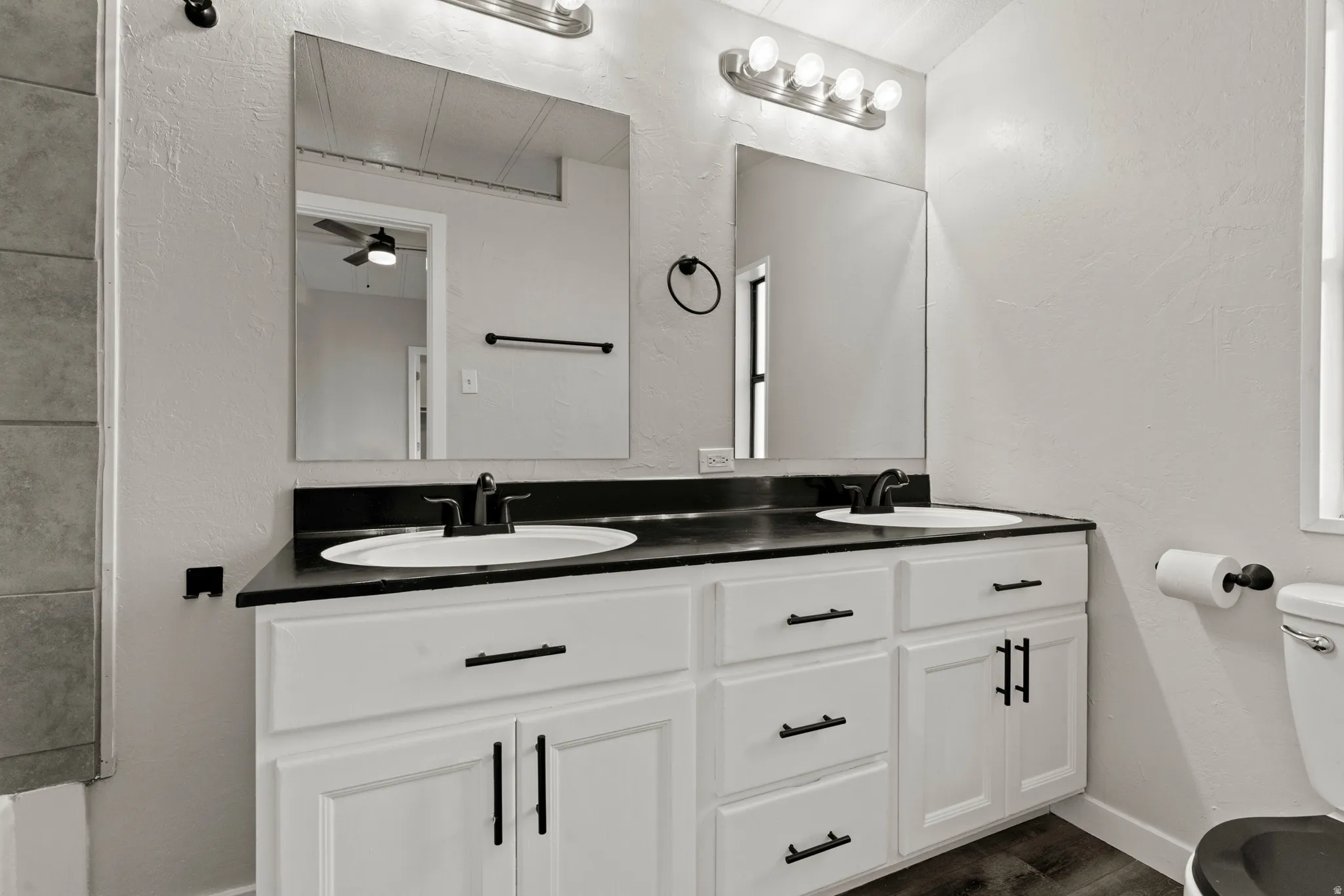 Full bathroom with a textured wall, double vanity, dark wood-type flooring, and ceiling fan
