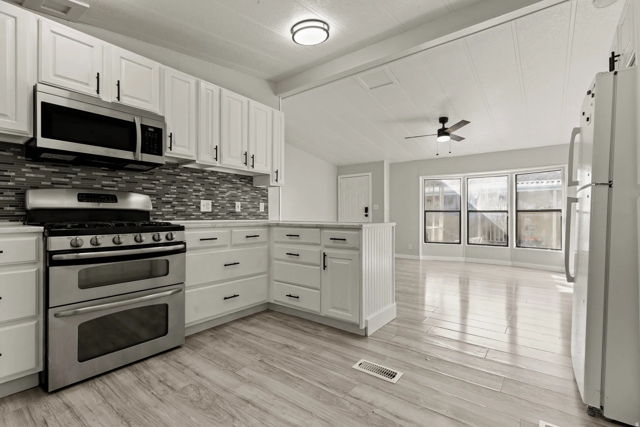 Kitchen featuring stainless steel appliances, light countertops, white cabinets, lofted ceiling with beams, and tasteful backsplash