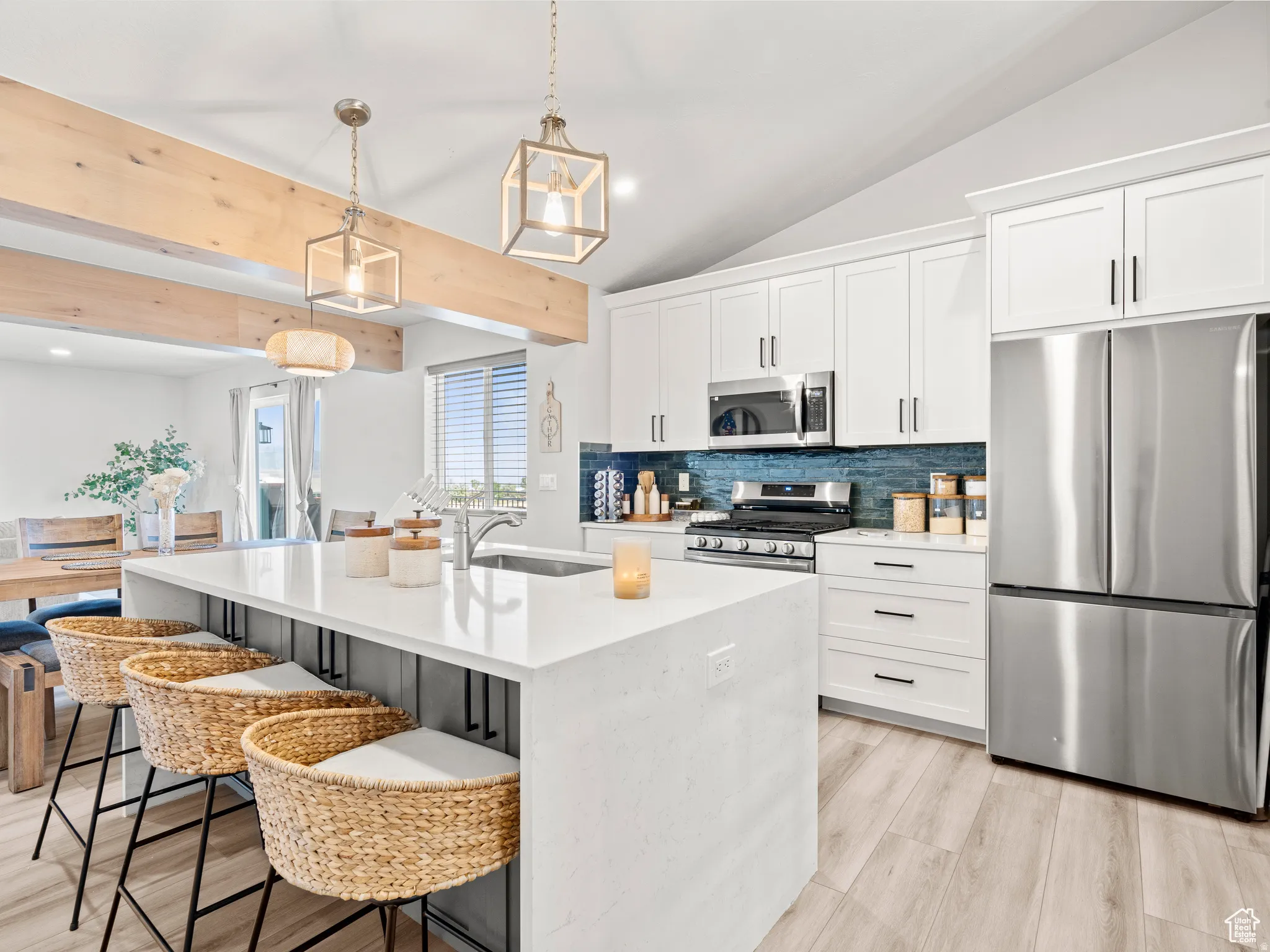 Kitchen with stainless steel appliances, decorative backsplash, modern hanging light fixtures, a kitchen breakfast oversized island bar, and  plenty of white cabinets