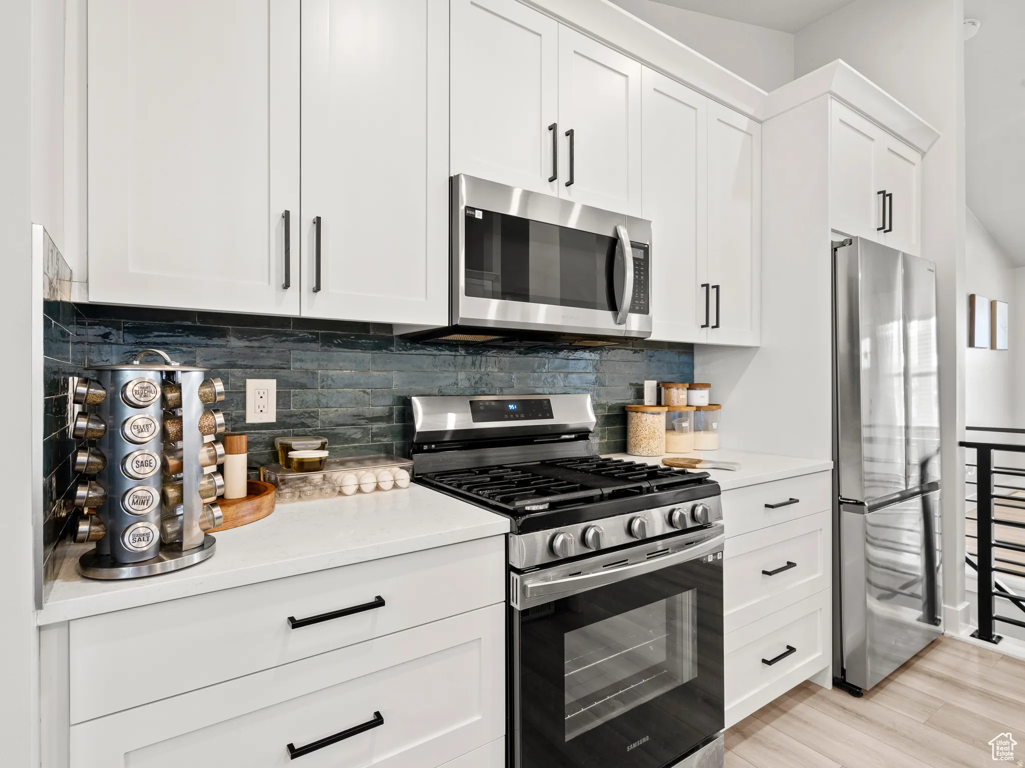 Kitchen with stainless steel appliances, white cabinetry, backsplash, light stone counters, and light wood-style flooring