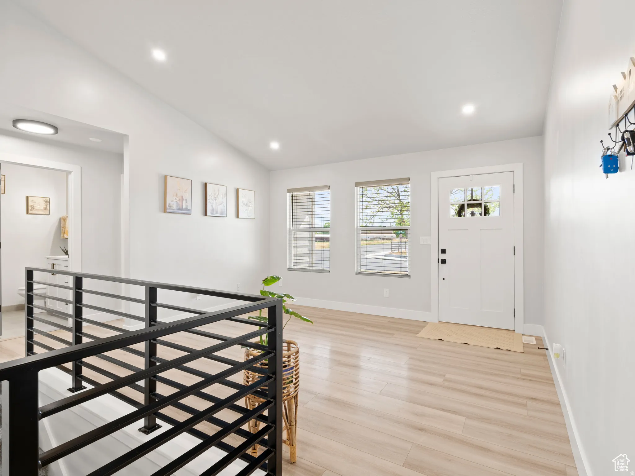 Entrance foyer featuring lofted vaulted ceiling, light wood-style floors, and recessed lighting, with black steel stair railing.