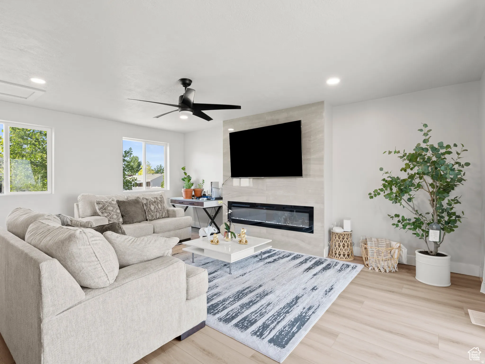 Living area with light wood-style floors, a large fireplace, ceiling fan, and recessed lighting