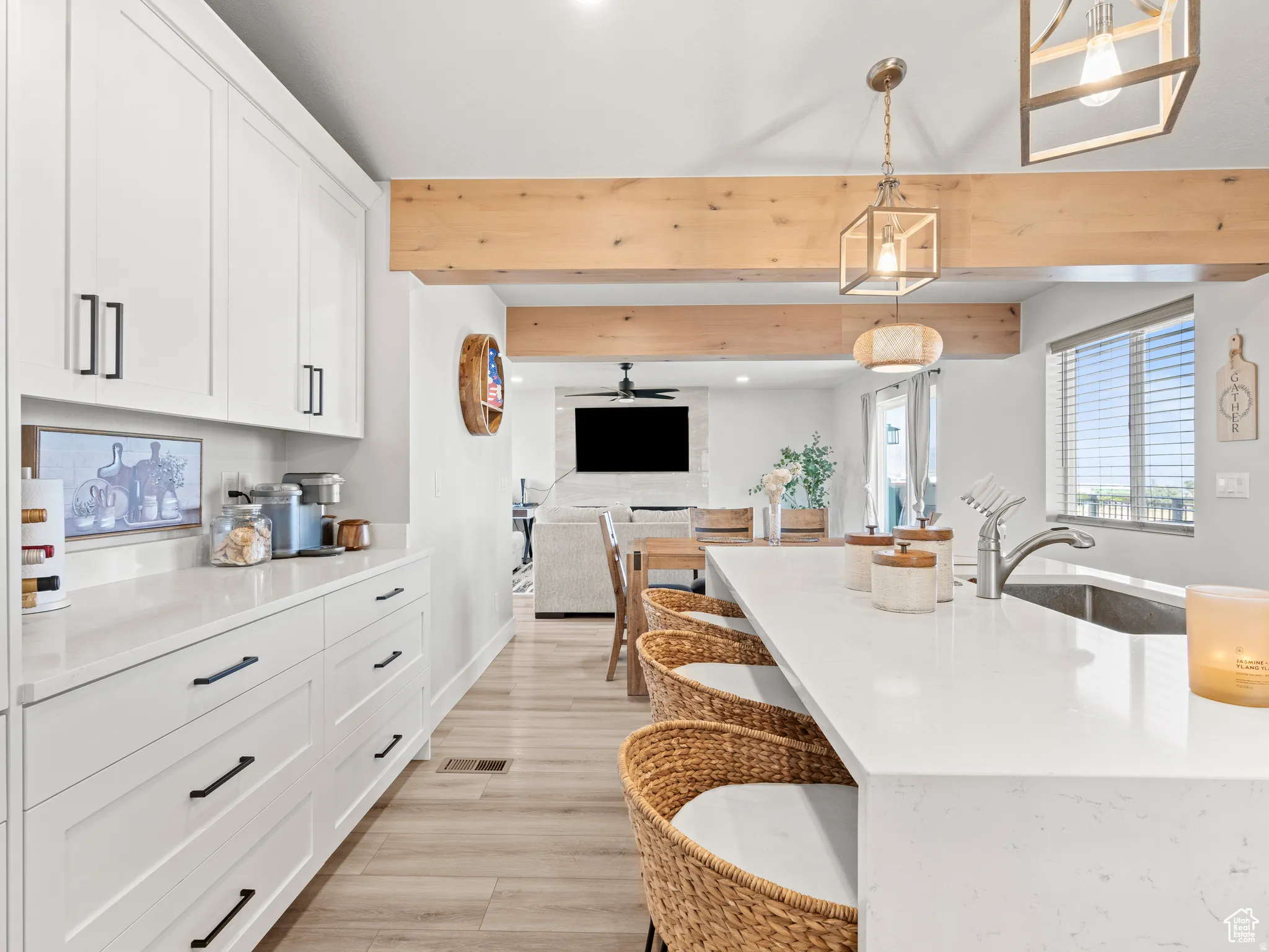 Kitchen featuring open floor plan, pendant lighting, light quartz counters, extra white cabinetry for more storage, and beamed ceiling