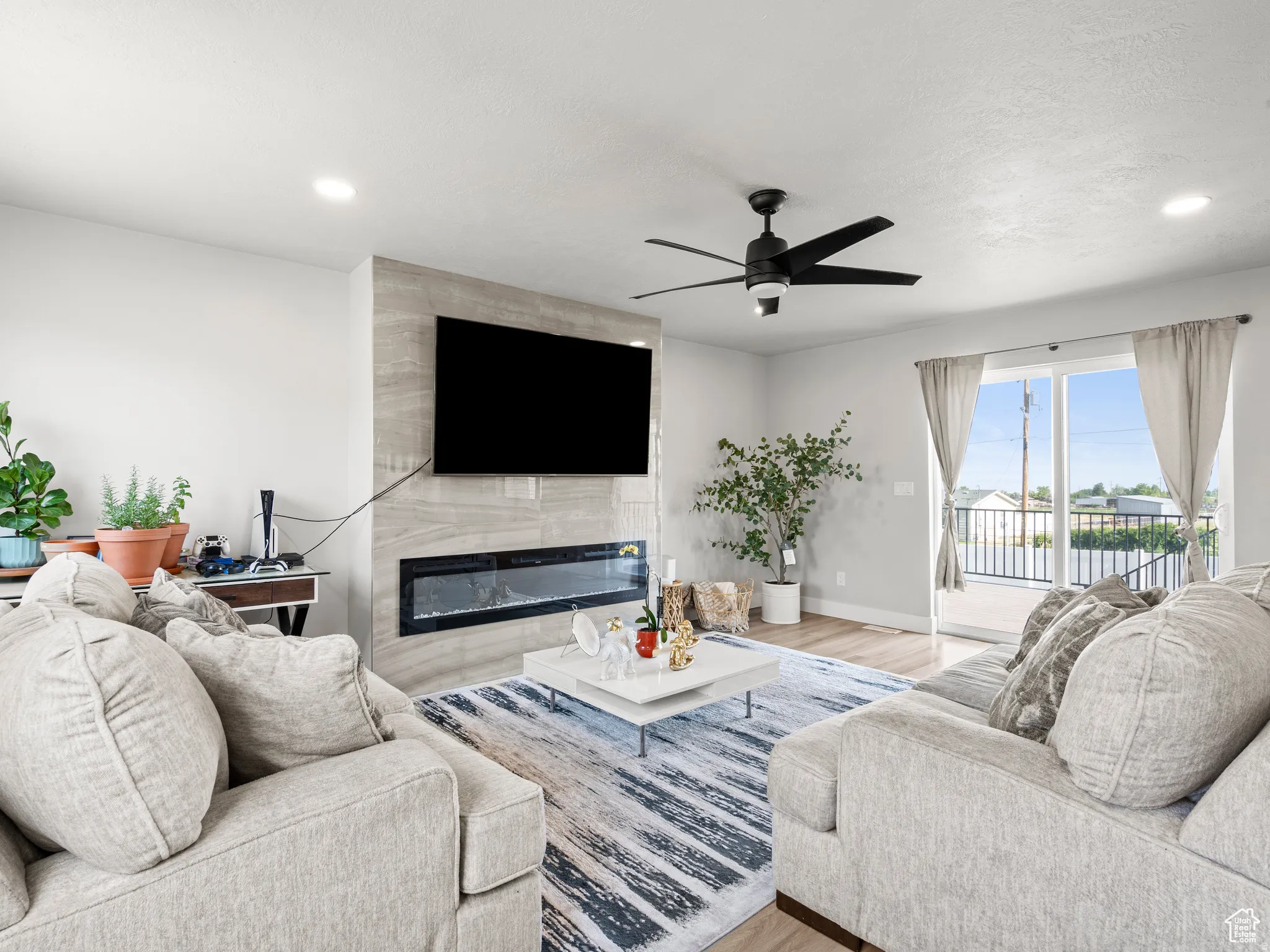 Living room with ceiling fan, a premium modern fireplace, light wood-style flooring, and recessed lighting