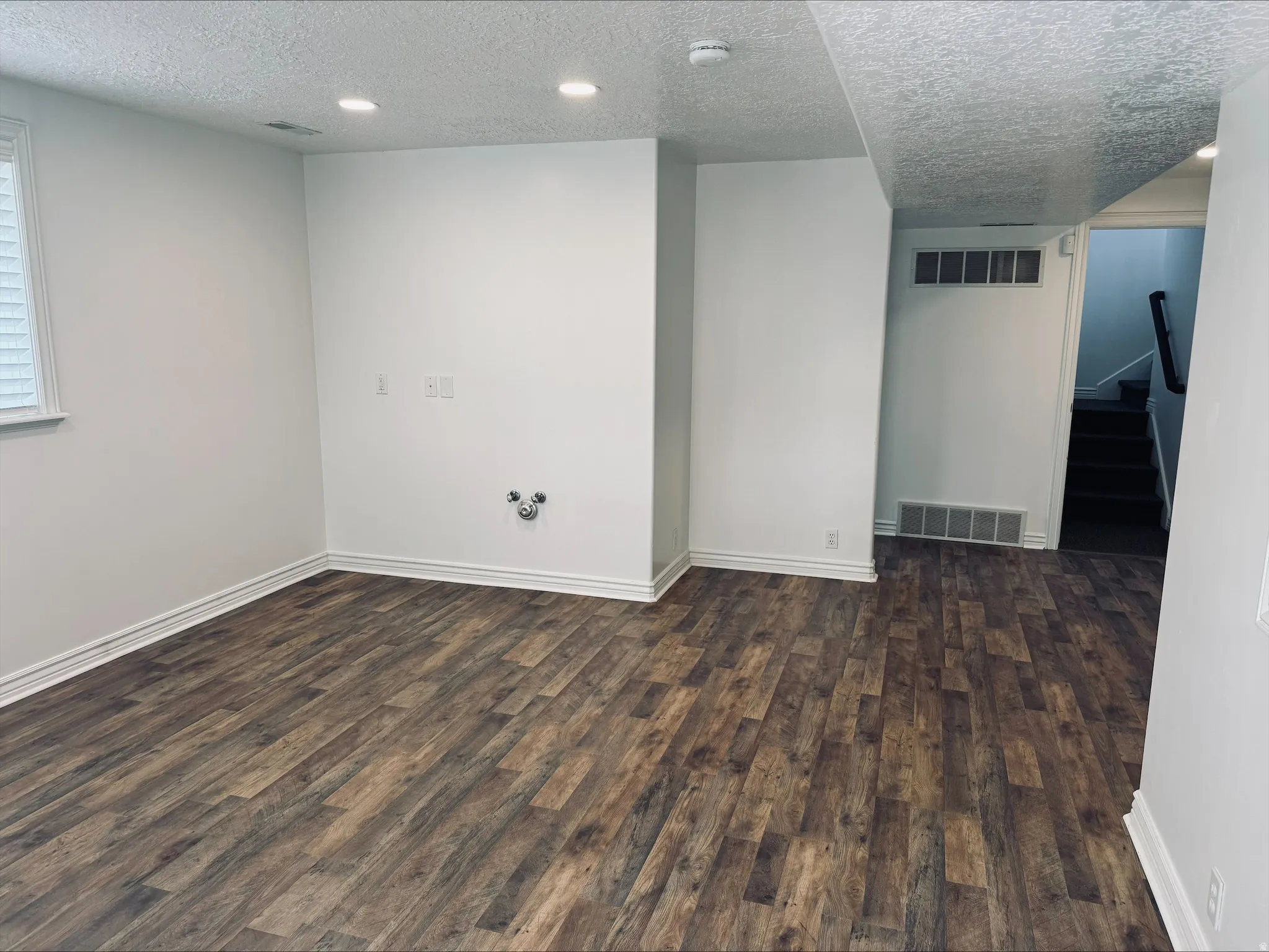 NEW FLOORS IN THE BASEMENT.Spacious room featuring wood-finish flooring, white walls, recessed lighting, and a visible window with blinds