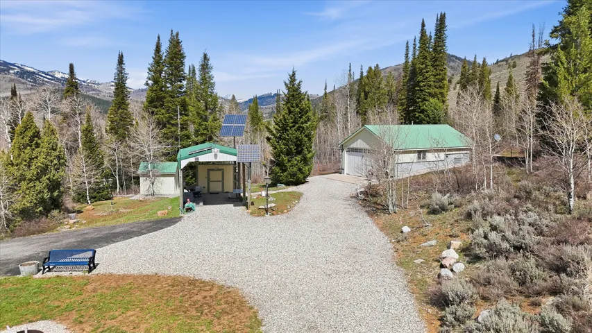 View of front facade featuring solar panels, a mountain view, an outbuilding, gravel driveway, and a garage