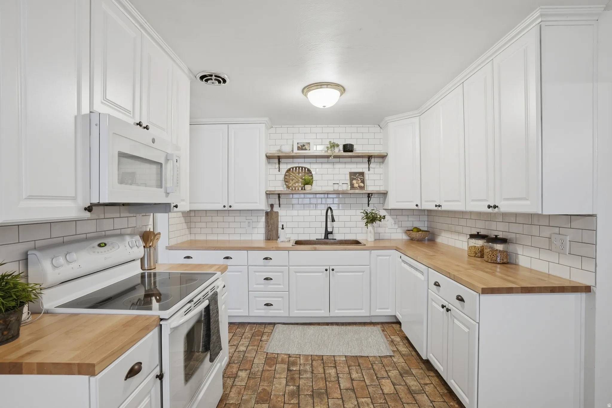 Kitchen with white appliances, open shelves, wood counters, white cabinets, and brick patterned floors