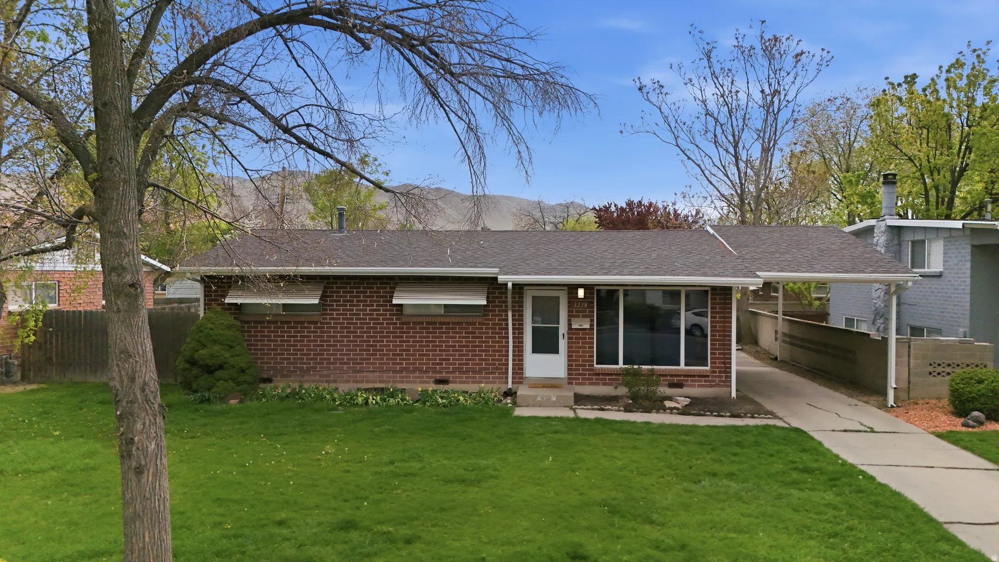 Ranch-style home featuring roof with shingles, brick siding, an attached carport, and driveway