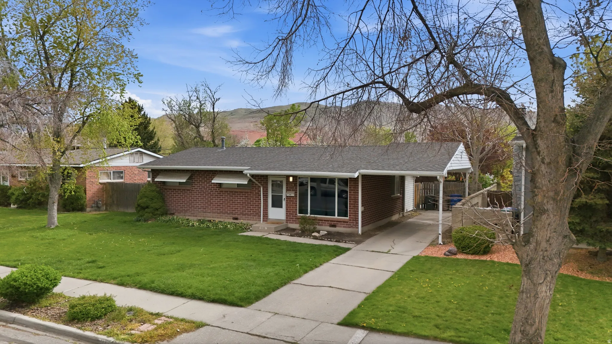 View of front facade with brick siding, concrete driveway, a carport, roof with shingles, and crawl space