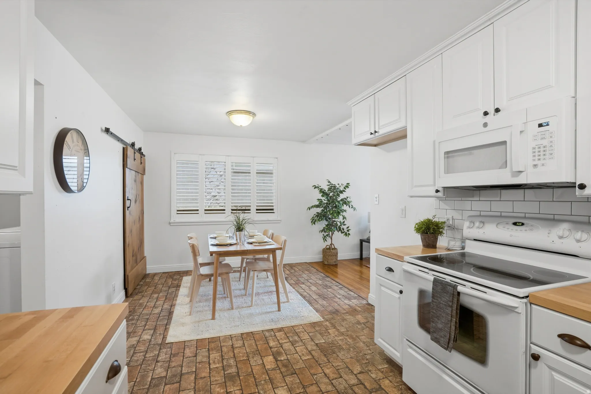 Kitchen with a barn door, white appliances, brick flooring, and white cabinets