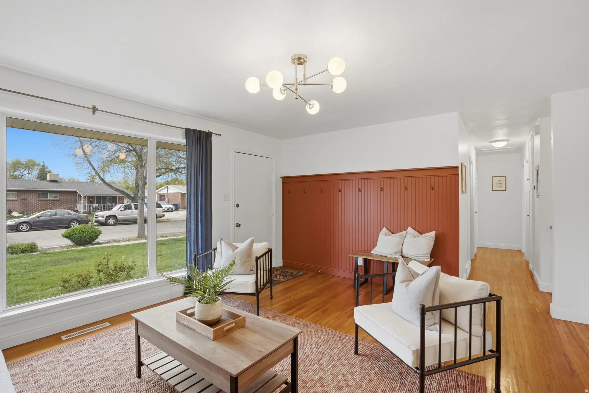 Living area with light wood-style flooring, hanging lights, and a residential view