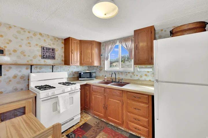 Kitchen featuring wallpapered walls, white appliances, wood finish cabinetry, and a textured ceiling