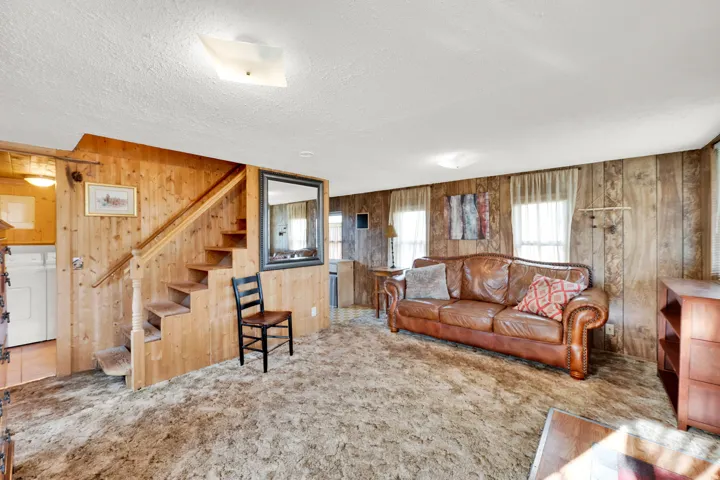 Living area with light carpet, wood walls, washer / clothes dryer, and a textured ceiling