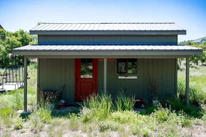 Compact structure featuring olive green vertical siding, a striking red entry door with glass panel, and a covered porch area