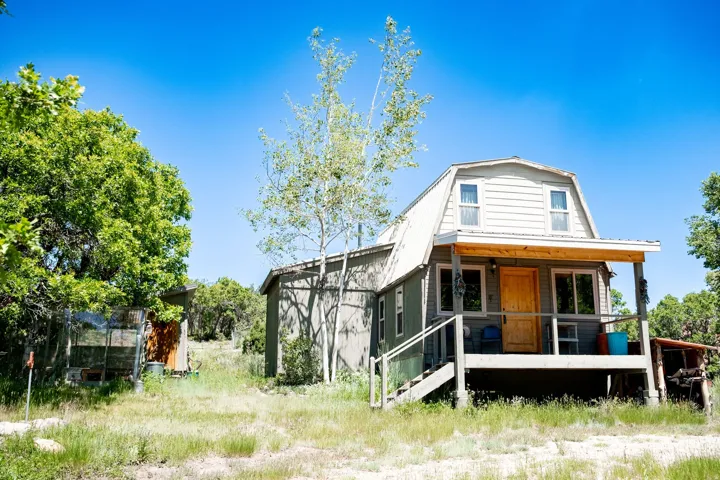 Gambrel roofline property featuring a covered front porch with natural wood posts, an exterior staircase, and a prominent natural wood entry door