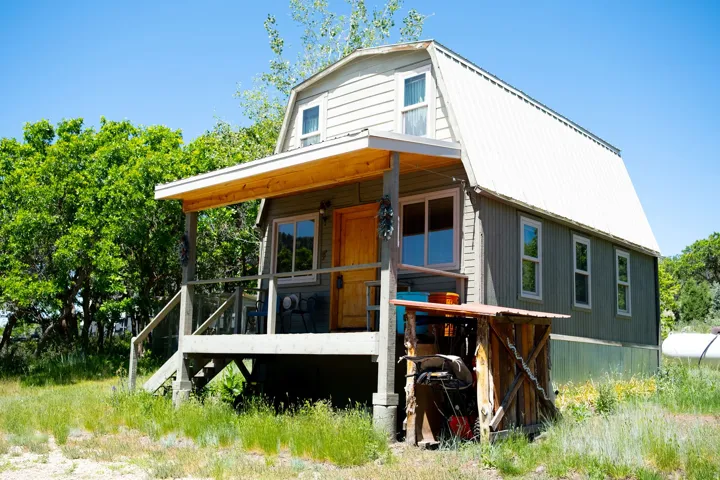 Gambrel-roofed residence featuring a covered front porch with a wood-plank ceiling, natural wood door, and multiple windows