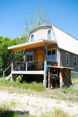 Gambrel-style residence featuring a covered wooden porch, light wood siding, and a metal roof