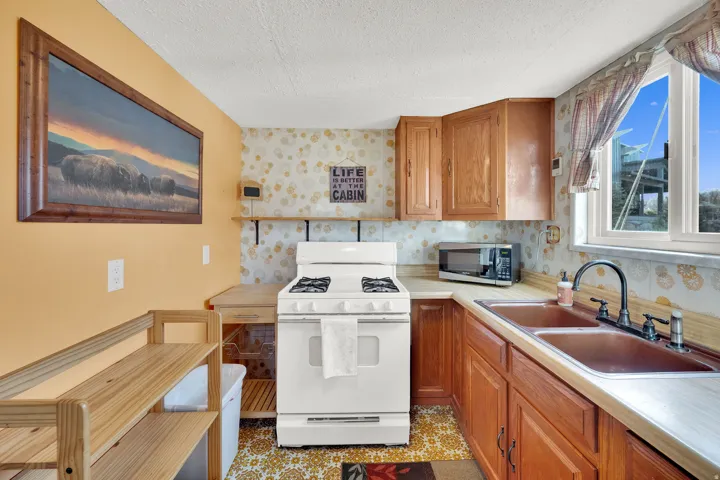 Kitchen with white range with gas cooktop, light countertops, wood finish cabinetry, wallpapered walls, and stainless steel microwave