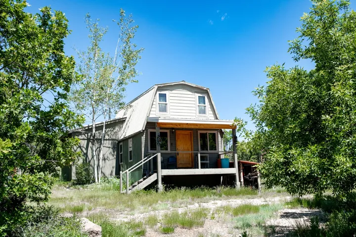 Gambrel-roofed residence featuring a covered front porch with exposed wood beams, a light wood-finish entry door, and a partially screened-in area