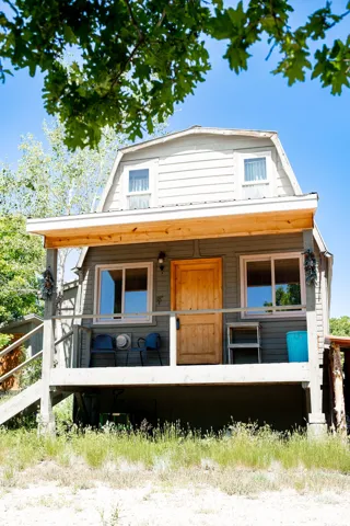 Gambrel roofline property featuring a front porch with a natural wood door, horizontal siding, and a wooden railing