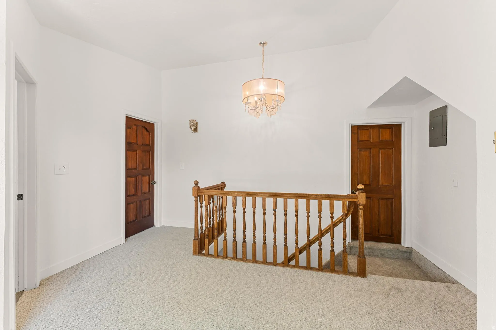 Corridor featuring an upstairs landing, light carpet, suspended lighting, electric panel, and vaulted ceiling