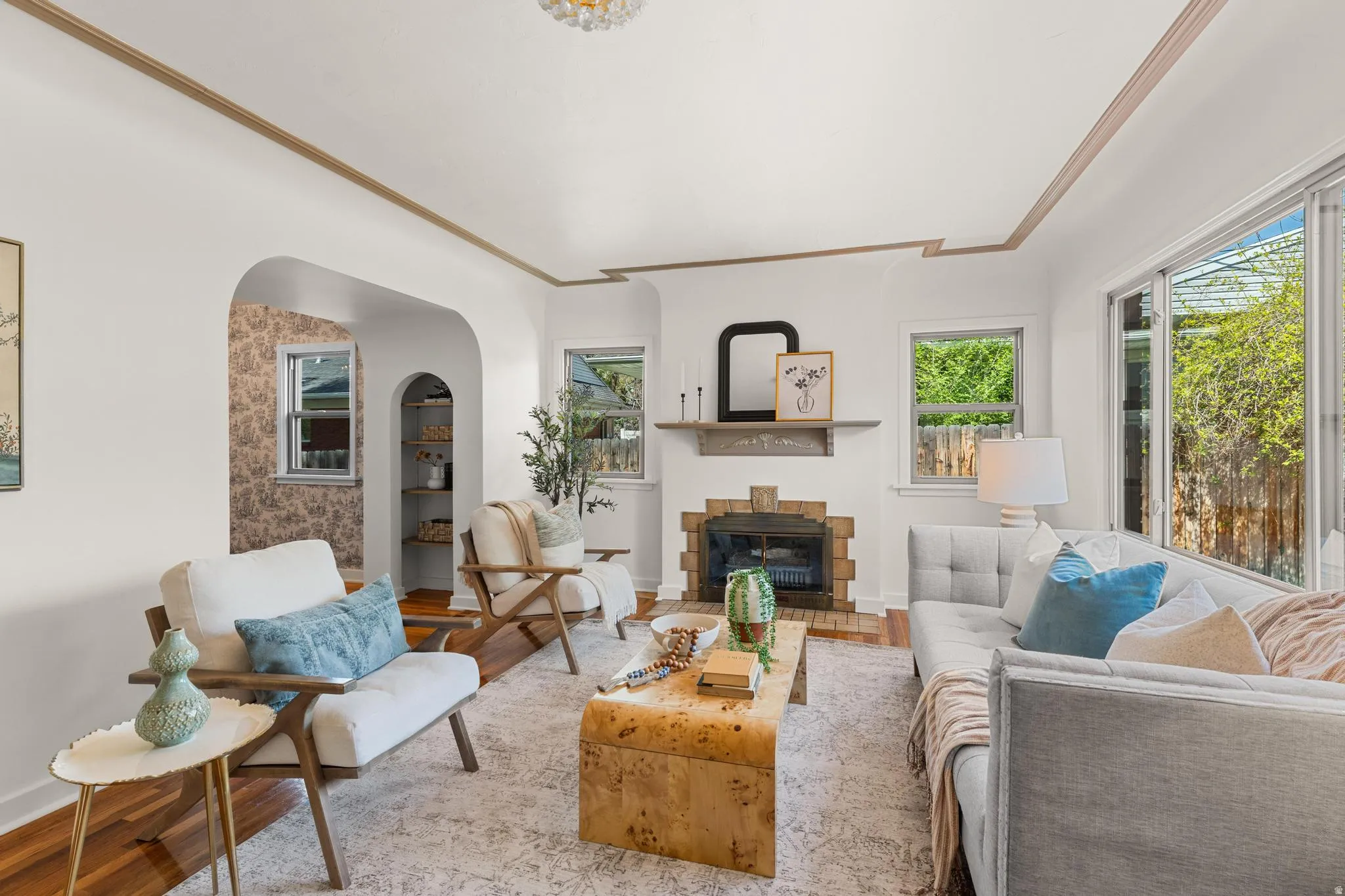 Living room featuring a glass covered fireplace, crown molding, wood finished floors, healthy amount of natural light, and arched walkways
