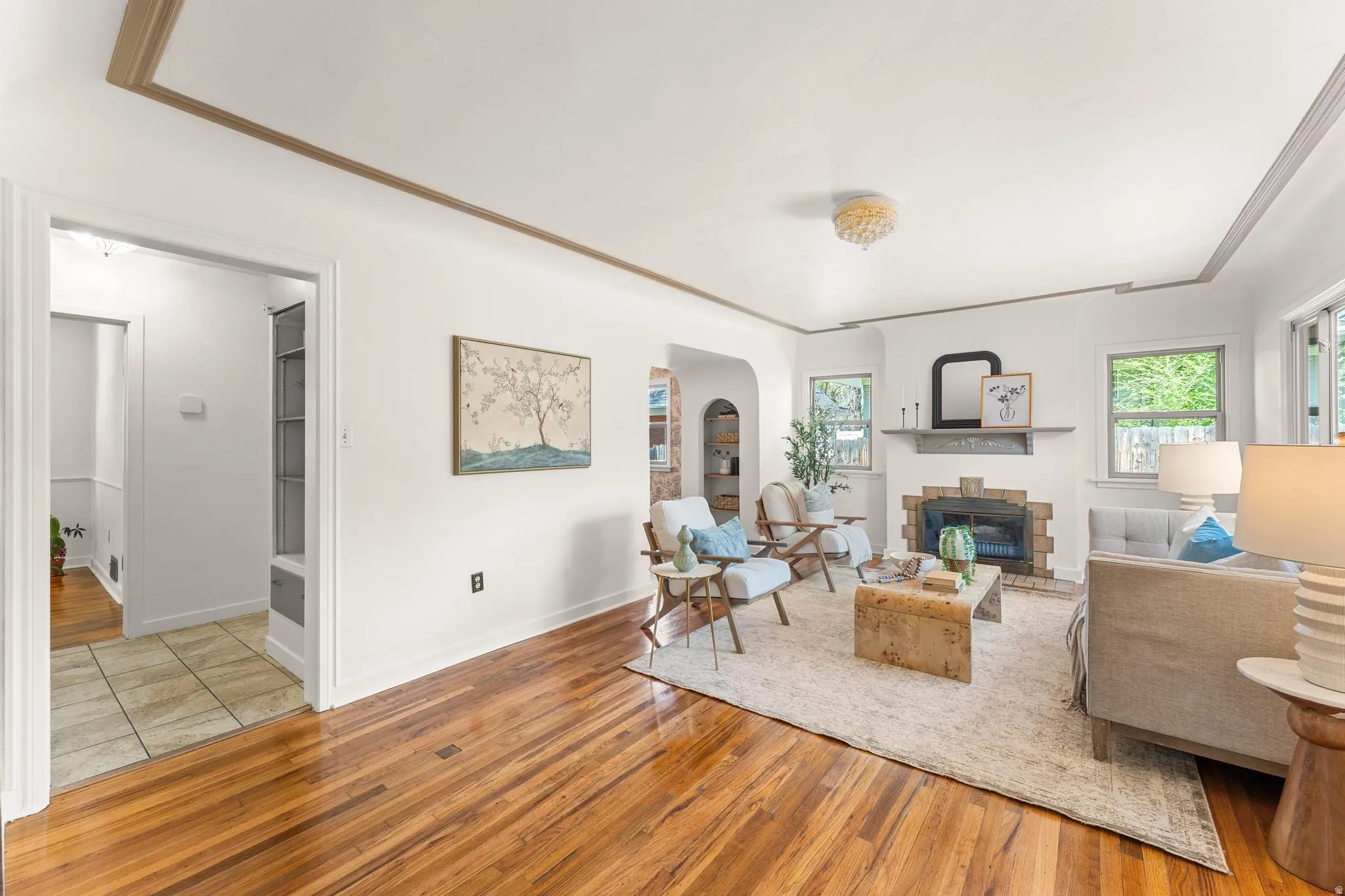 Living area with light wood-type flooring, arched walkways, a brick fireplace, and ornamental molding