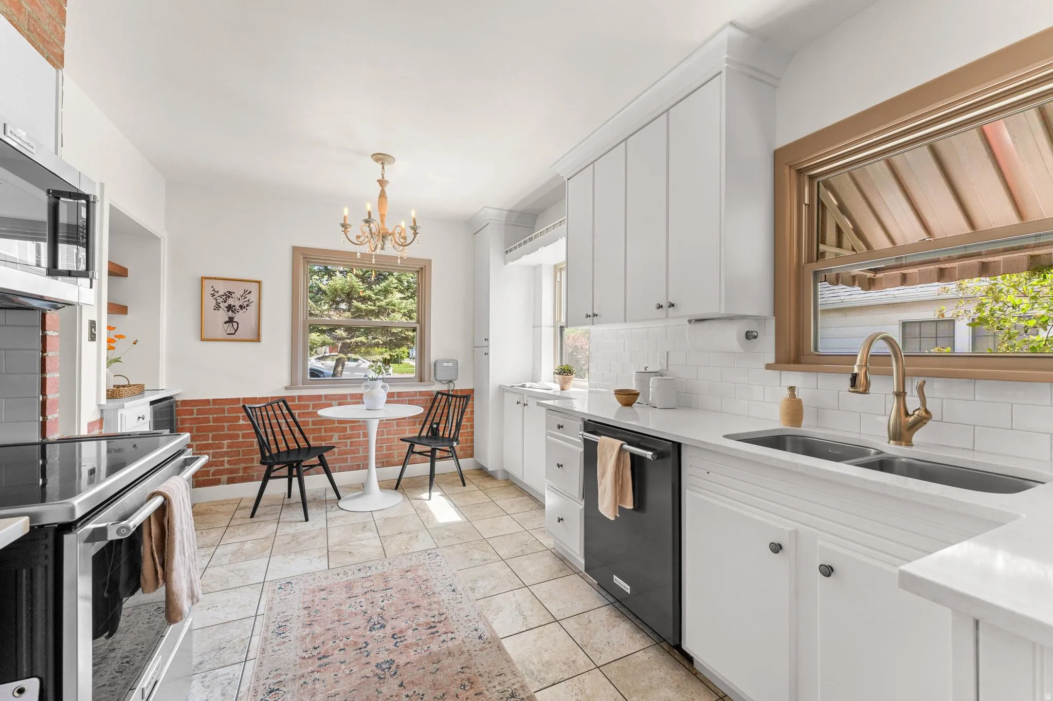 Kitchen featuring white cabinets, stainless steel appliances, light stone counters, brick wall, and a chandelier